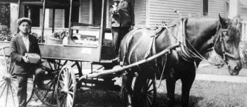 Two men with a horse and buggy, selling materials out of the back of the buggy.